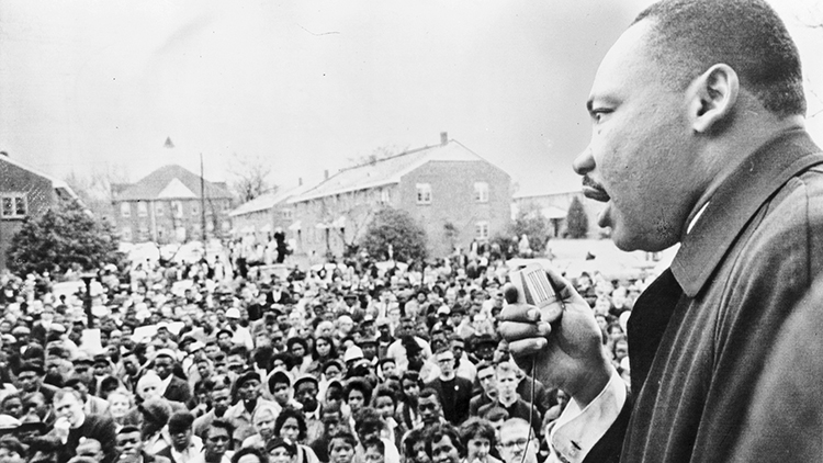 Martin Luther King, Jr. speaking into a microphone in front of a crowd.