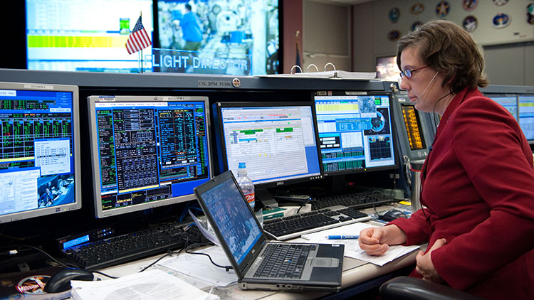 Scientiet at a computer, surrounded by monitors, communicating with astronauts in space.