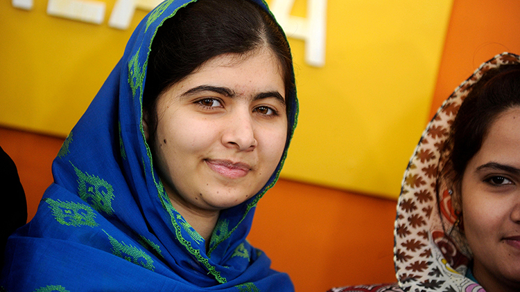 Malala Yousafzai in a blue and green head scarf standing against an orange and yellow background.