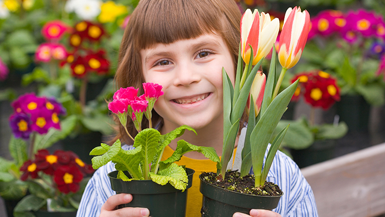 A girl smiling and holding a flower pot.