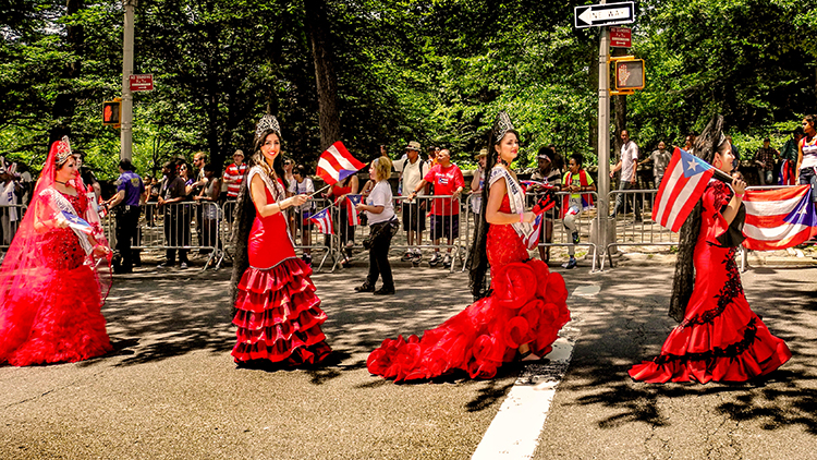 Traditionally dressed young ladies march proudly up Fifth Avenue in the New York Puerto Rican Day parade on a spring day in Manhattan, New York City. Note Puerto Rican flags