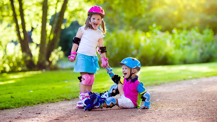 A girl and boy learn to roller skate in summer park.