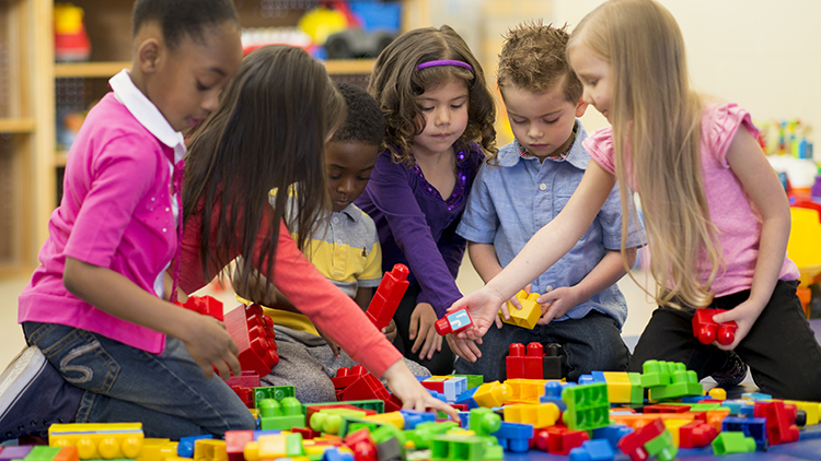 A multi-ethnic group of preschool children are playing together with colorful plastic blocks and are building towers.