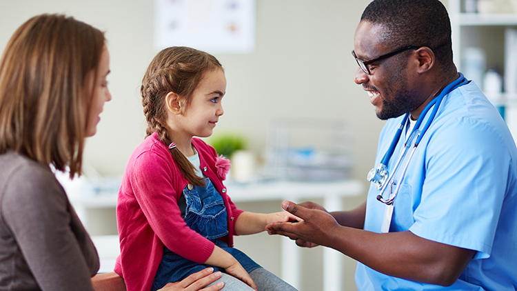 Seated view of a doctor talking to his young patient while her mother looks on in a doctor's office