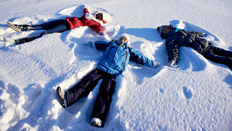 Familia juguetona haciendo ángeles de nieve.