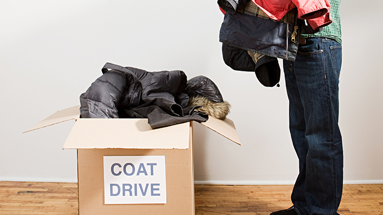 Full-length profile view of a man holding an armful of coats next to a full box for a coat drive