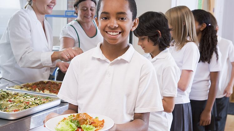Estudiante sosteniendo el plato de almuerzo en la cafetería de la escuela.
